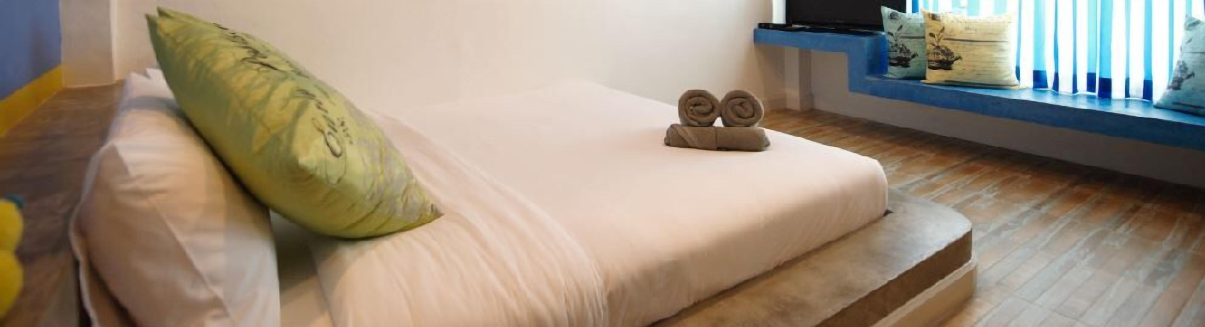 Una cama con un almohadón verde y dos toallas enrolladas encima.