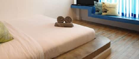 Una cama con un almohadón verde y dos toallas enrolladas encima.