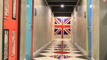 A hallway with a checkered floor, doors with red and blue frames, and a Union Jack flag on the wall.