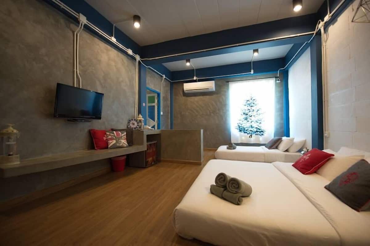 Quarto de hotel moderno com televisão de tela plana, escrivaninha de madeira, sofá e cama com toalhas dobradas.