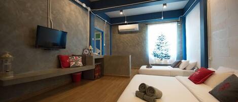 A modern hotel room with a flat-screen TV, a wooden desk, a sofa, and a bed with rolled towels.