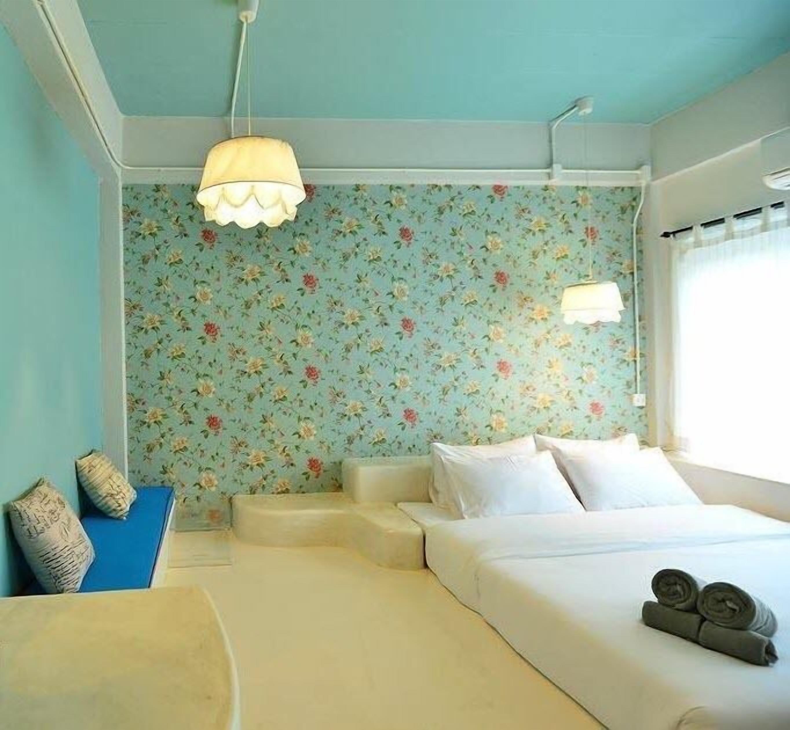 A bedroom with a floral wallpaper, a bed with white linens, a blue chair, and a hanging light fixture.