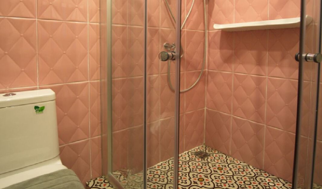 A bathroom with pink diamond-patterned tiles, a shower enclosure, and a patterned floor.