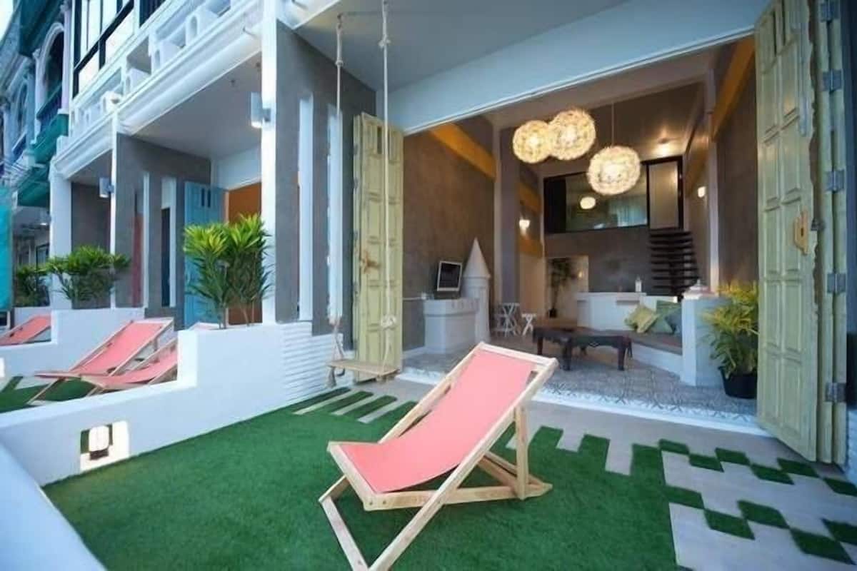 Um saguão de hotel com balcão de recepção, área de estar e um lounge à beira da piscina com uma cadeira vermelha.