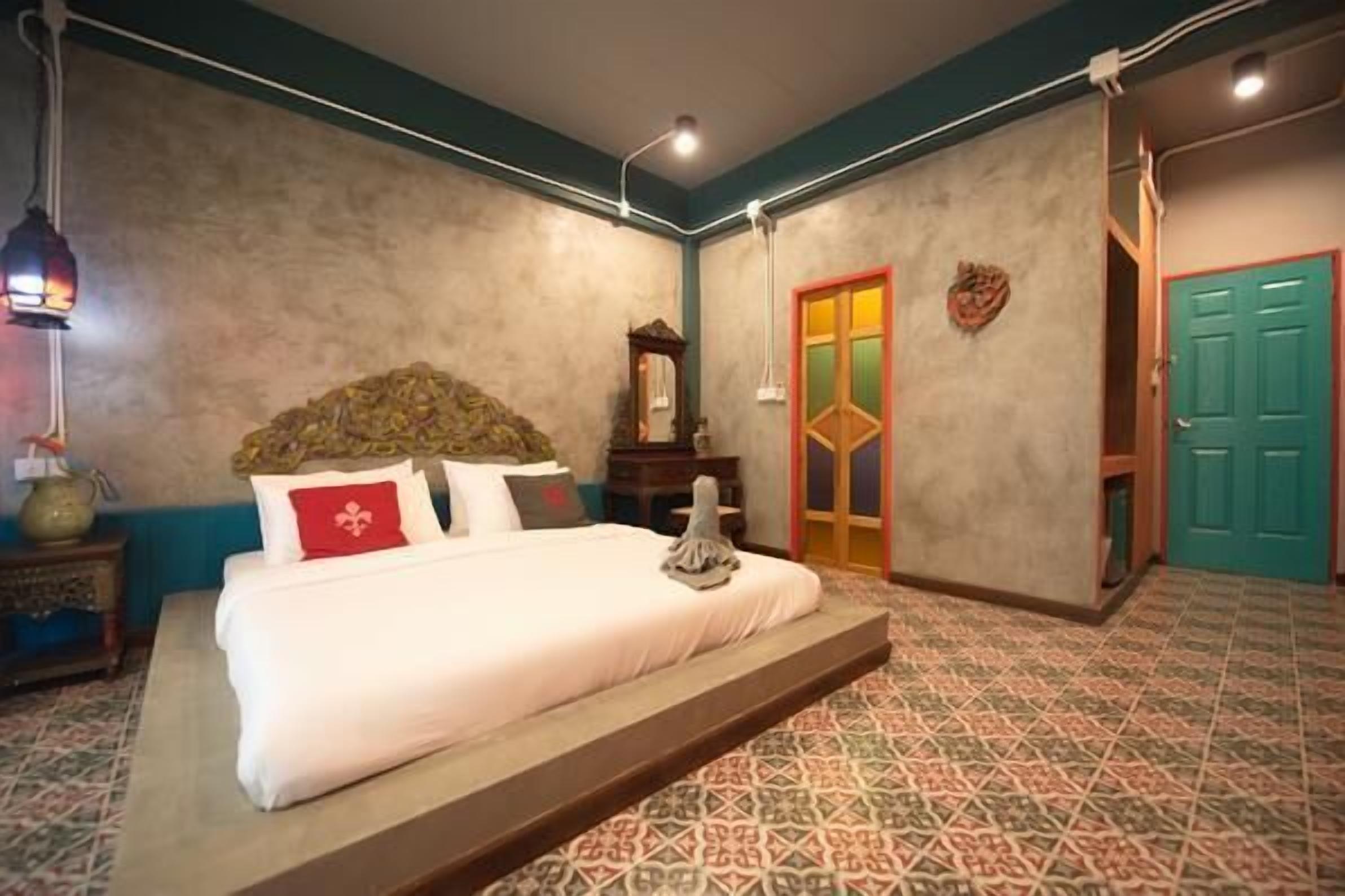 A bedroom with a bed, a nightstand, a wall-mounted lamp, a mirror, and a door with a colorful frame.