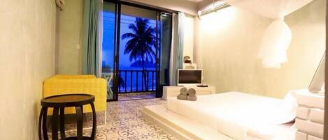 A hotel room with a bed, a small table, a TV, and a balcony with a view of palm trees.
