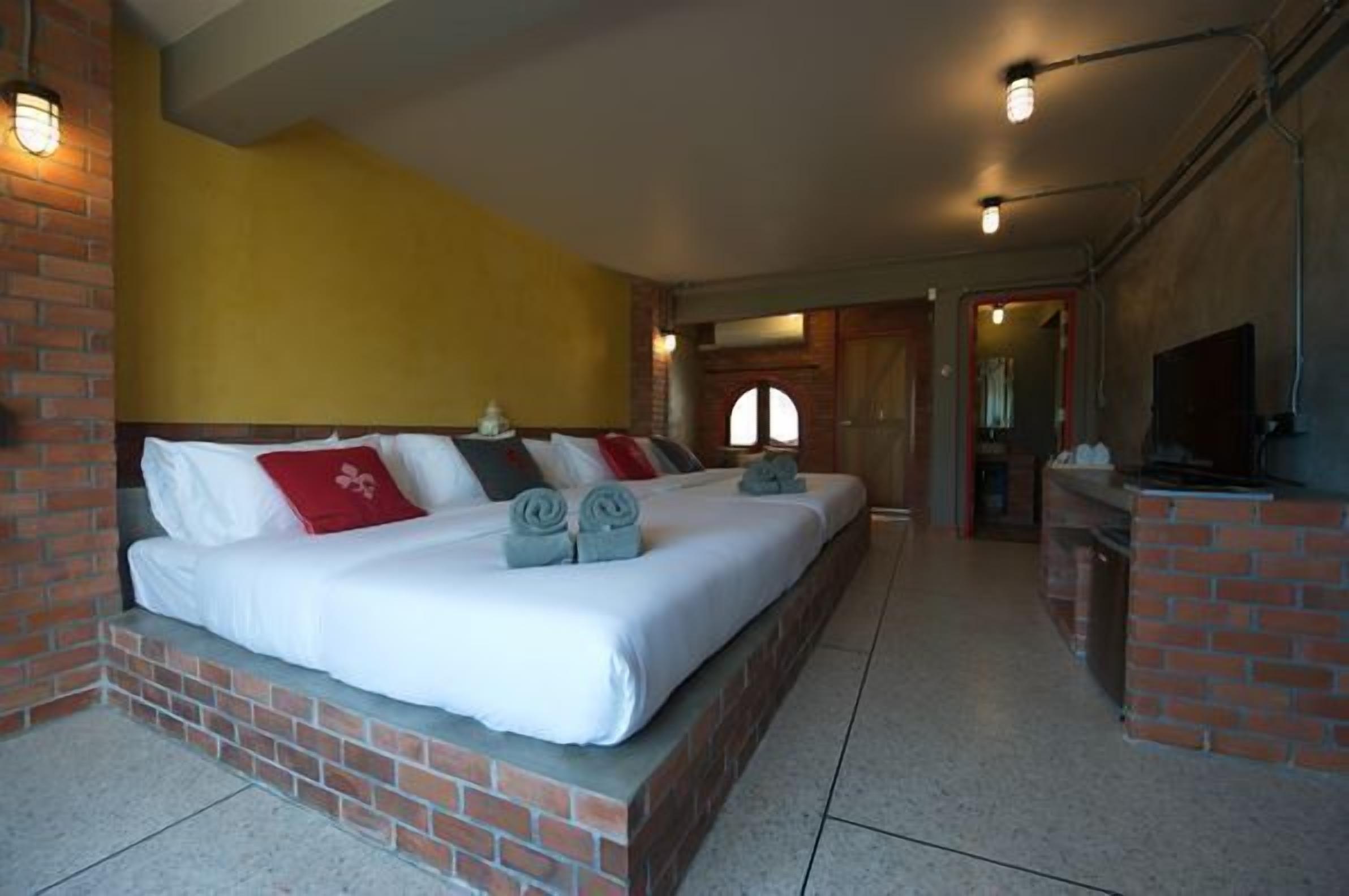 A bedroom with a brick fireplace, a bed with white bedding, and a TV mounted on the wall.