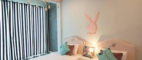 A hotel room with two beds, a chandelier, striped curtains, and a wall decoration.
