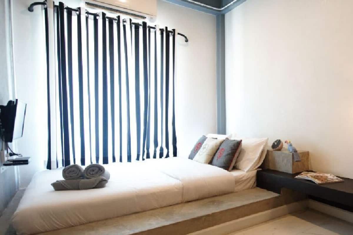 Quarto com cama, escrivaninha, laptop e janela com cortinas.