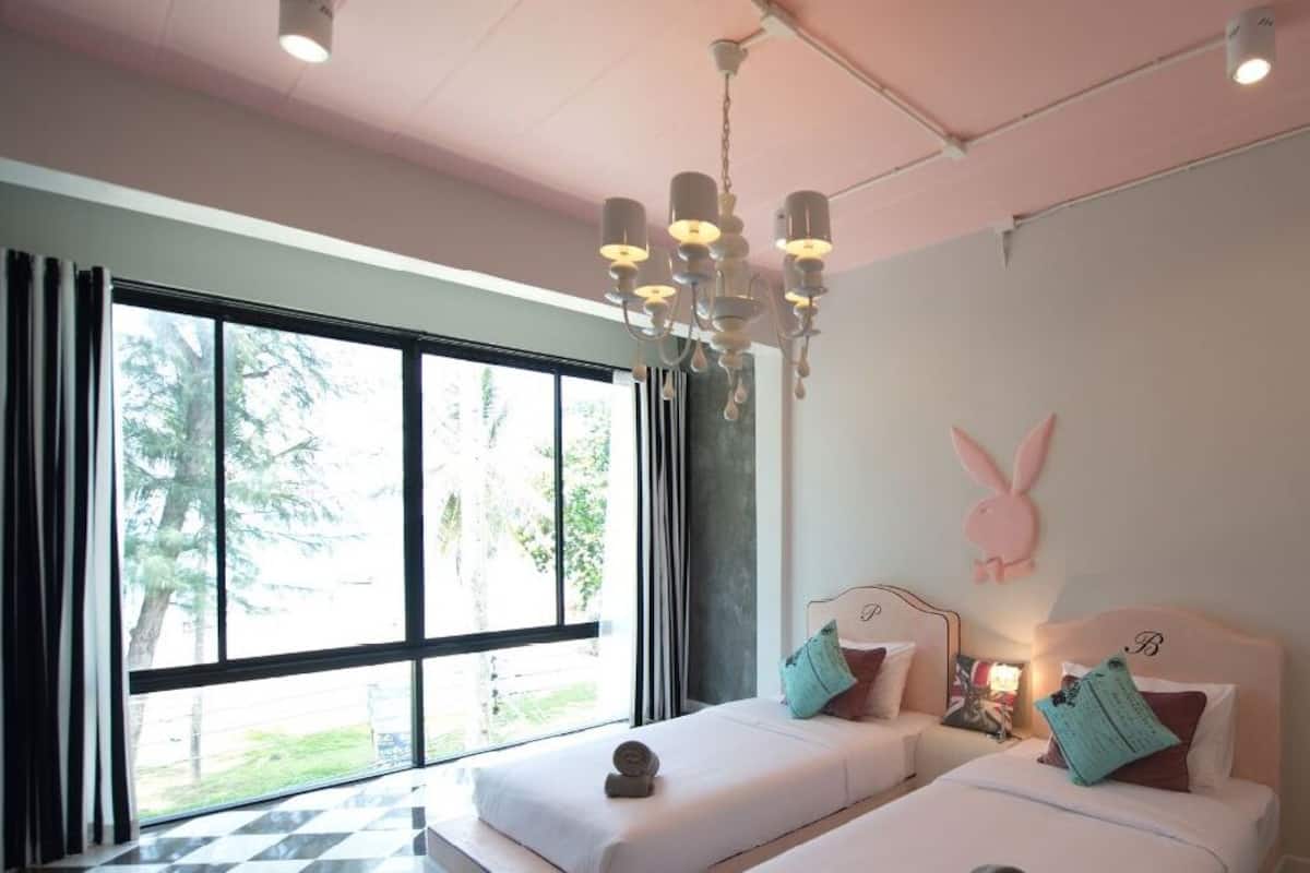 Quarto com duas camas, um candelabro, uma janela grande e uma decoração de coelho na parede.