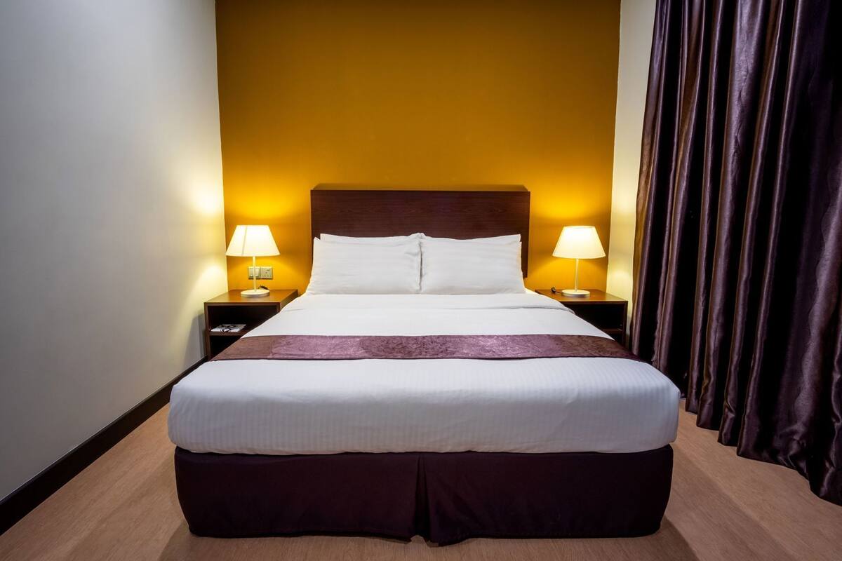 A hotel room with a large bed, two bedside tables with lamps, a wooden headboard, and a curtain on the right side.