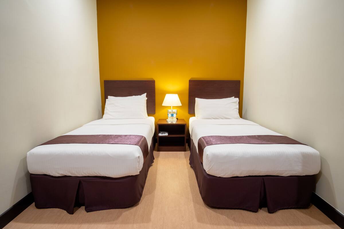 A hotel room with two beds, a nightstand with a lamp, and a yellow accent wall.