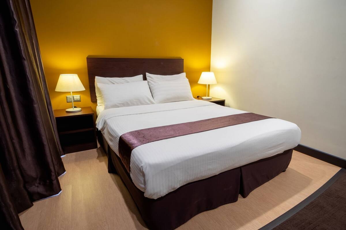 A hotel room with a bed, two bedside lamps, a nightstand, and a curtain.