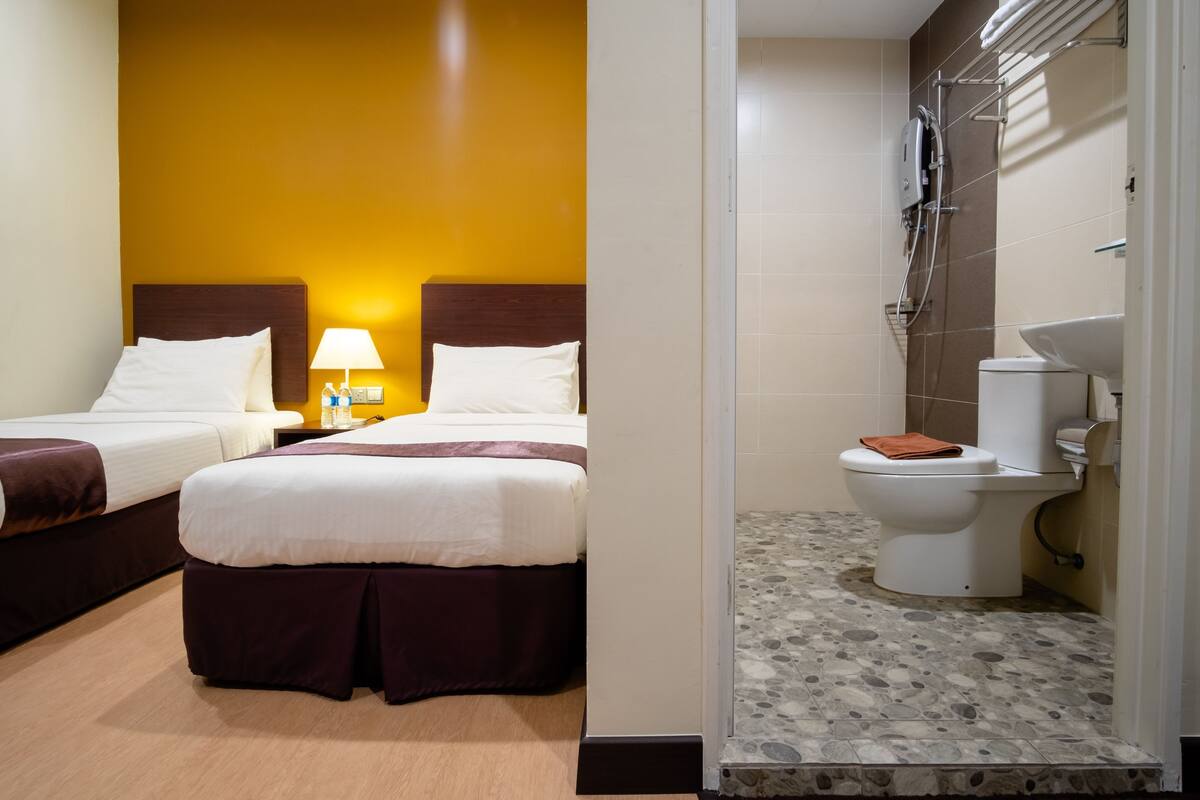 A hotel room with two beds, a bathroom with a shower, and a toilet.