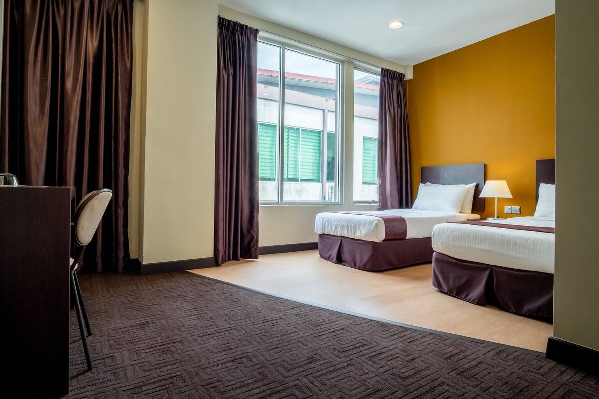A hotel room with two beds, a desk, and a window with curtains.