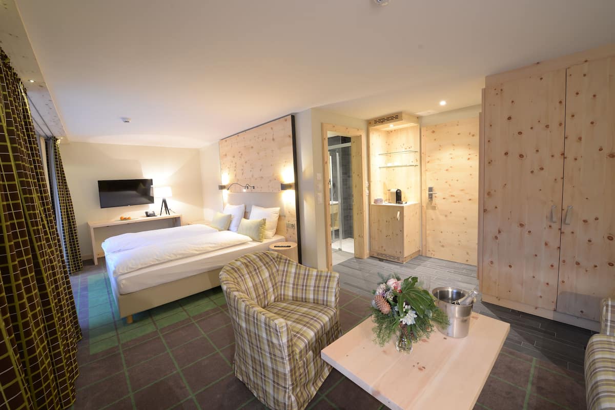 A hotel room with a bed, a chair, a table with a vase of flowers, a TV, and a wooden wardrobe.