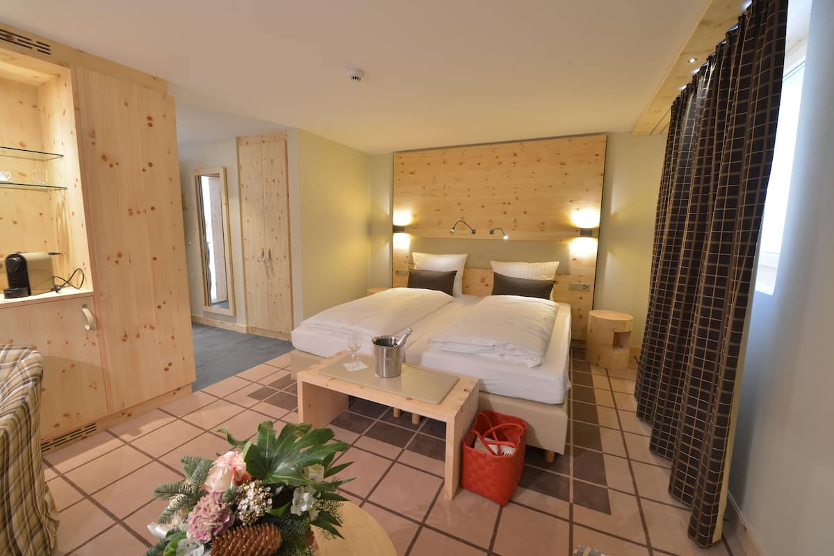 A hotel room with a wooden headboard, a bed with white linens, a bedside table with a lamp, a red basket, and a small plant on the floor.