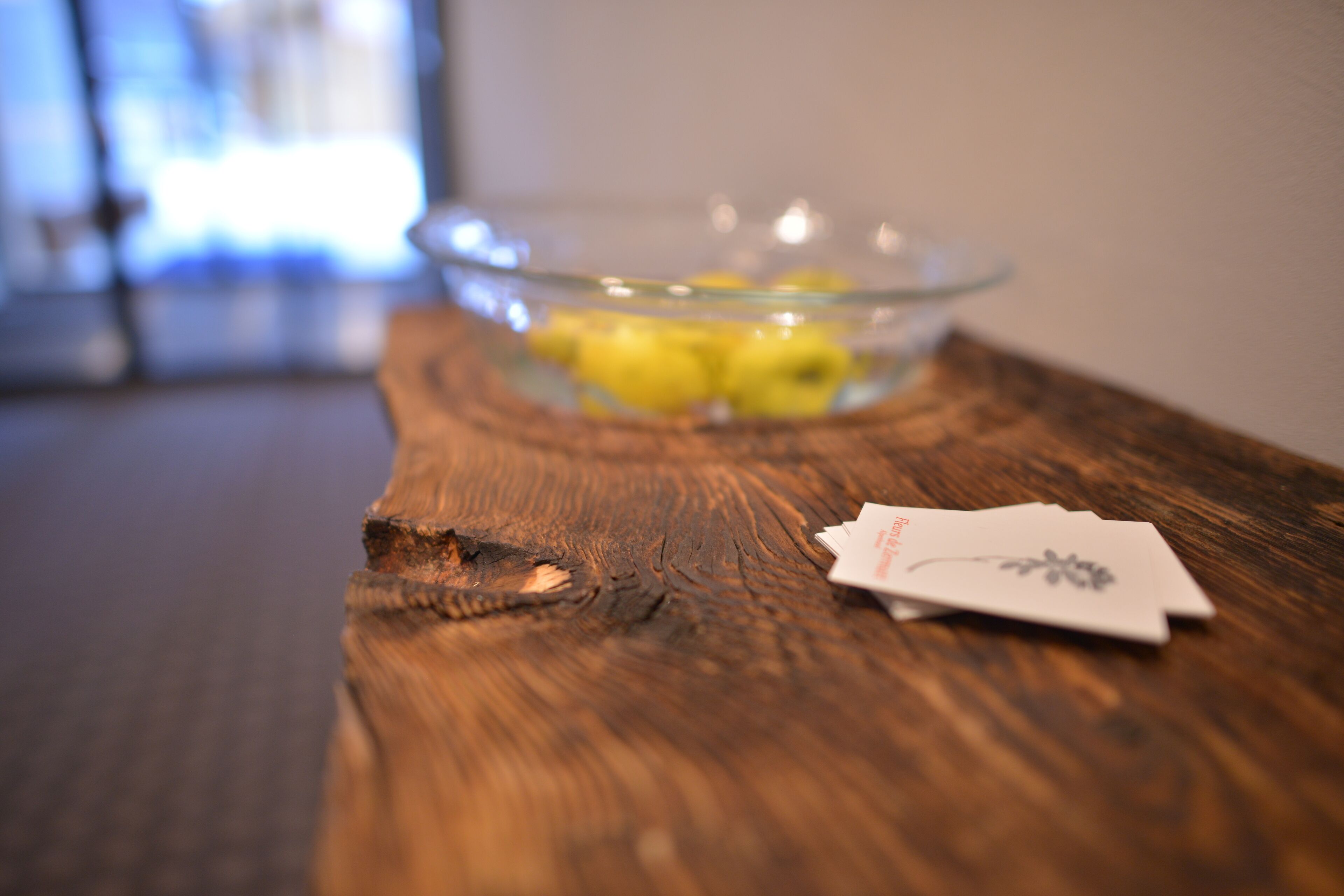 A wooden table with a glass bowl containing lemons and a card.