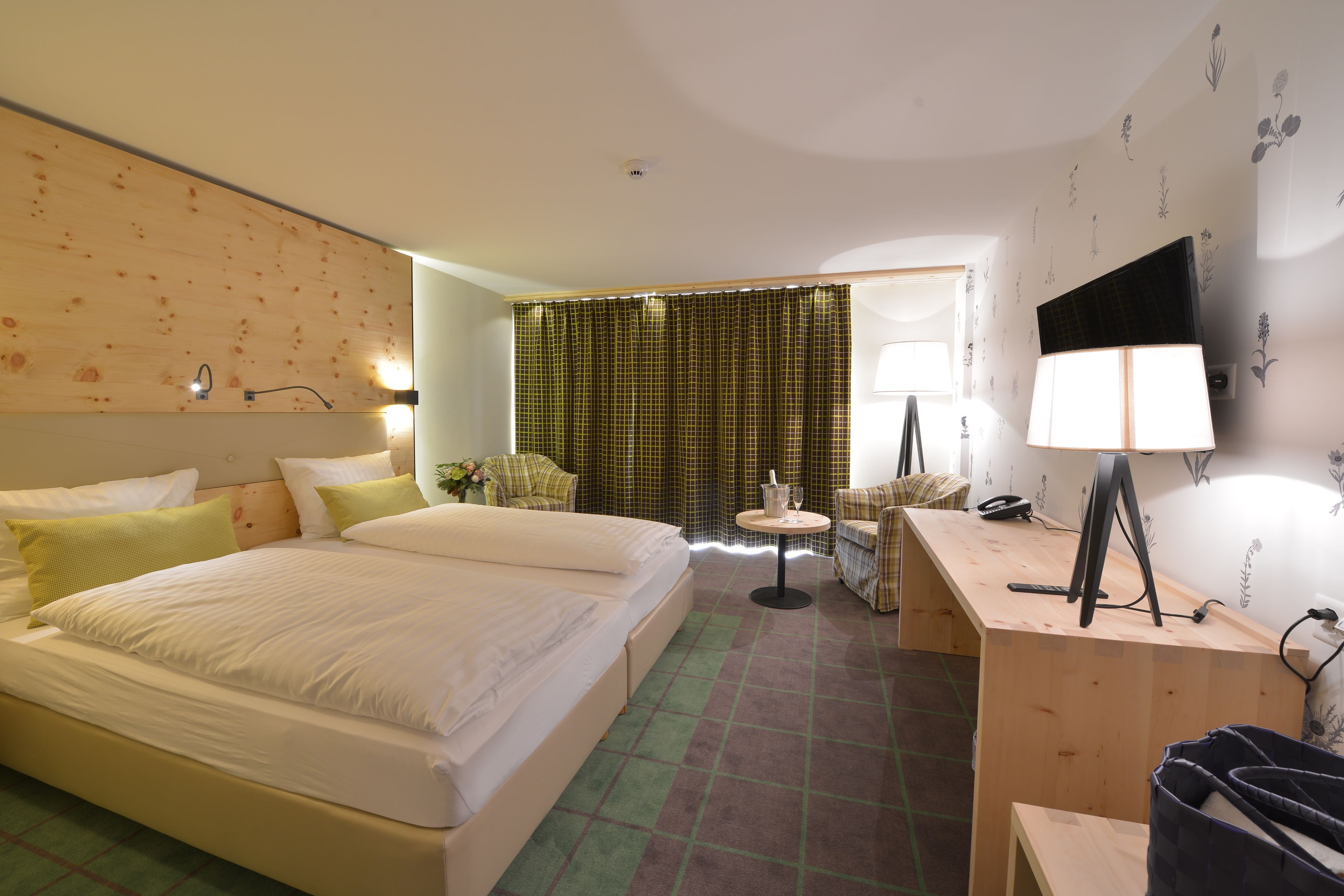 A hotel room with a large bed, a desk with a computer, a chair, and a small table with a lamp.