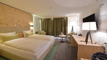 A hotel room with a large bed, a desk with a computer, a chair, and a small table with a lamp.