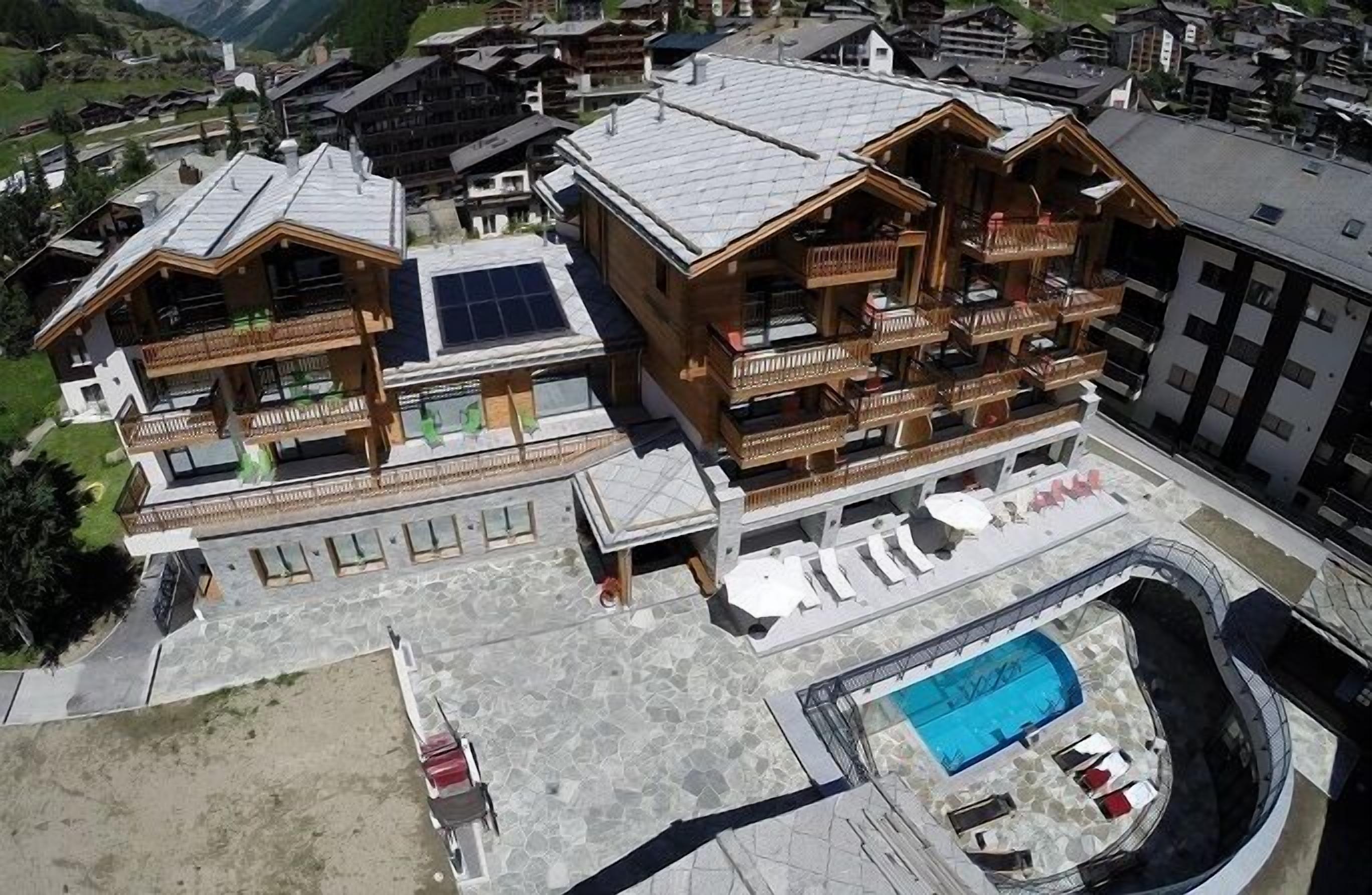 A large wooden chalet with multiple balconies, a swimming pool, and a ski lift visible in the background.