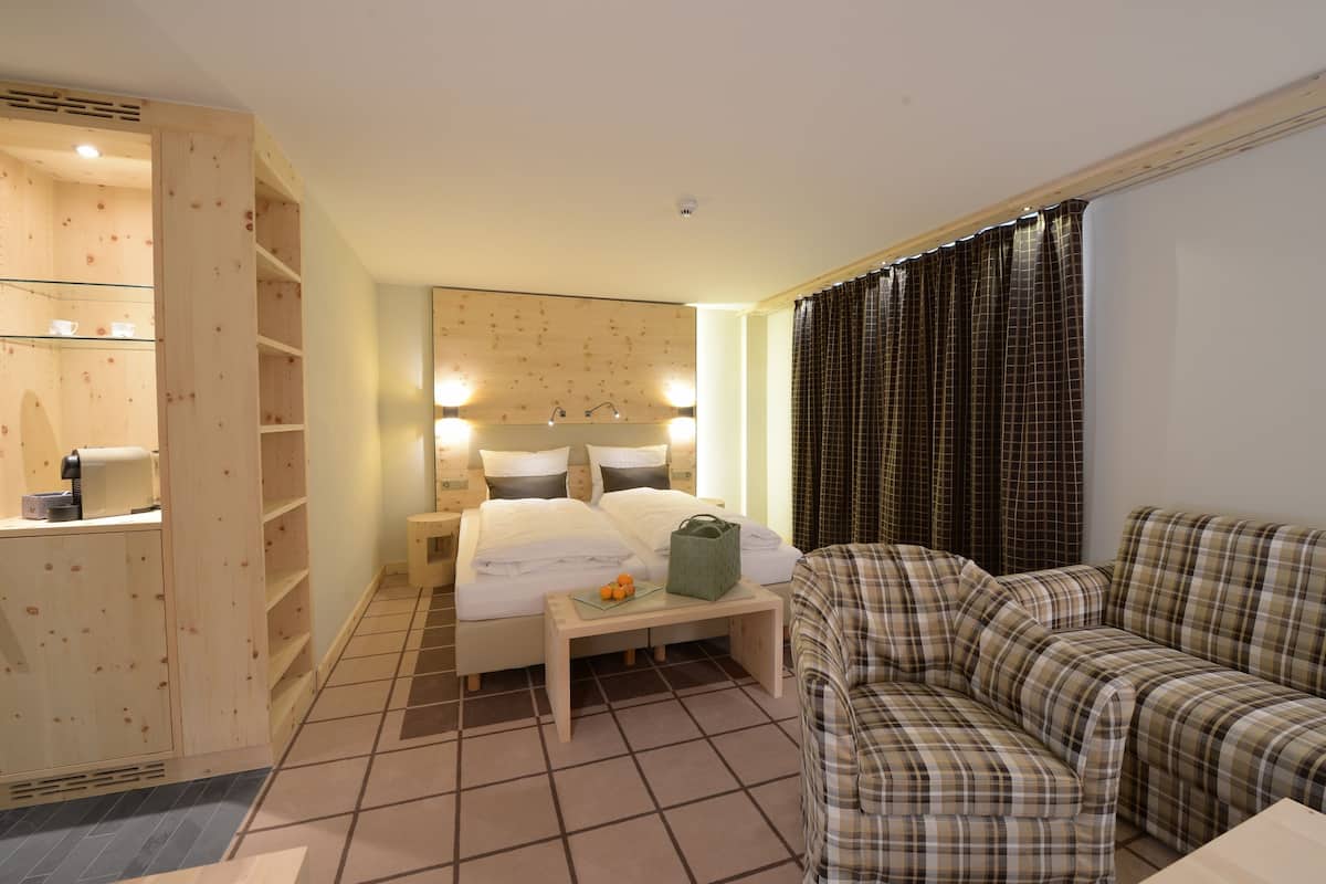A hotel room with a bed, a wooden wardrobe, a sofa, and a small table with a basket and oranges.