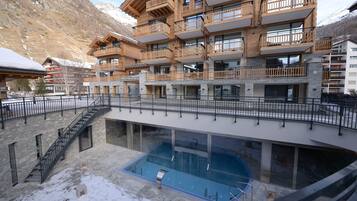Un hotel de varios pisos con zona de piscina, balcones de madera y montañas al fondo.