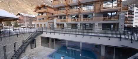 A multi-story hotel with a pool area, wooden balconies, and a mountainous backdrop.