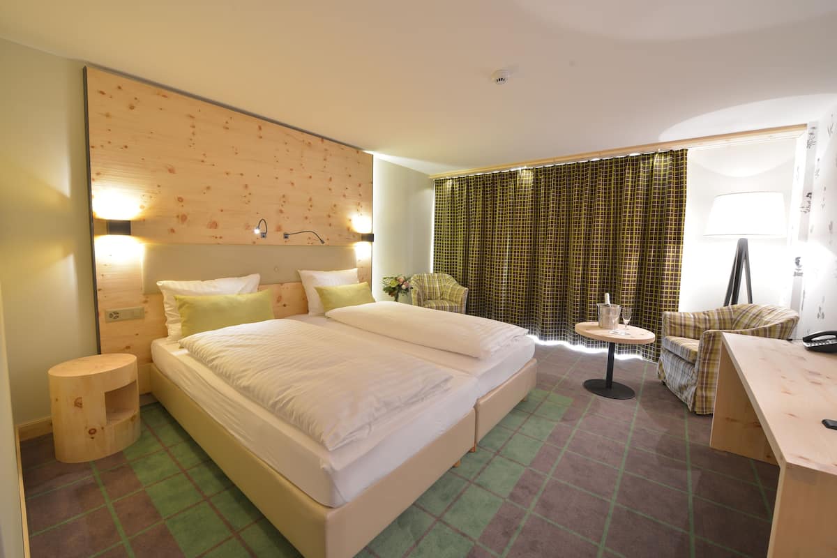 A hotel room with a large bed, a small round table, a chair, and a desk with a lamp.