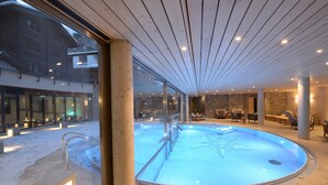 A modern indoor pool with clear glass walls, wooden ceiling, and stone flooring. - Alpenhotel Fleurs de Zermatt (Zermatt)