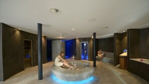A modern spa area with a circular seating area, a reception desk, and a large pillar. - Alpenhotel Fleurs de Zermatt (Zermatt)