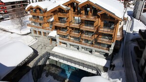 A multi-story wooden building with balconies, a ski lift, and a pool area. - Alpenhotel Fleurs de Zermatt (Zermatt)