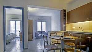 A compact hotel room with a kitchenette, a dining area with a table and chairs, and a separate living area with a sofa and a window. - Palatia Village (Hersonissos)