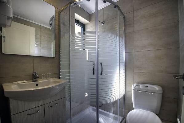 A modern bathroom with a glass-enclosed shower, a white sink, and a toilet. - Palatia Village (Hersonissos)