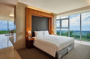 A modern hotel room with a large bed, a nightstand, and a view of the landscape.