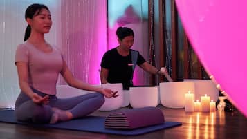 Dos personas meditando sobre esterillas de yoga en una habitación con velas y un globo rosa grande.