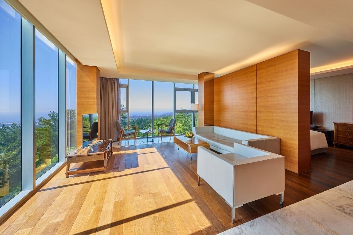 A modern hotel room with a large window, a sofa, a desk, and a chair.