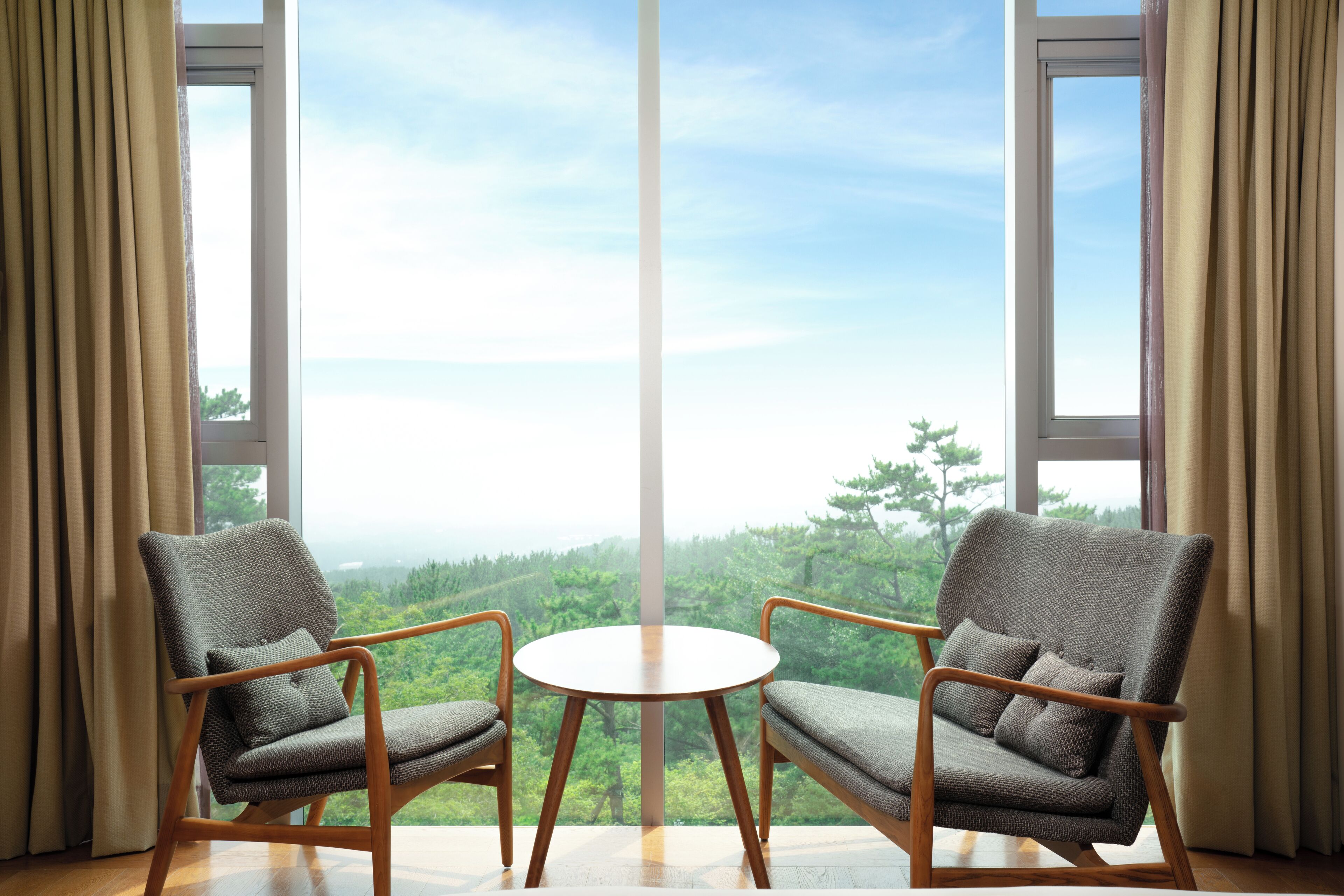 Una habitación con dos sillones y una pequeña mesa, ventanas amplias con vistas a un bosque.
