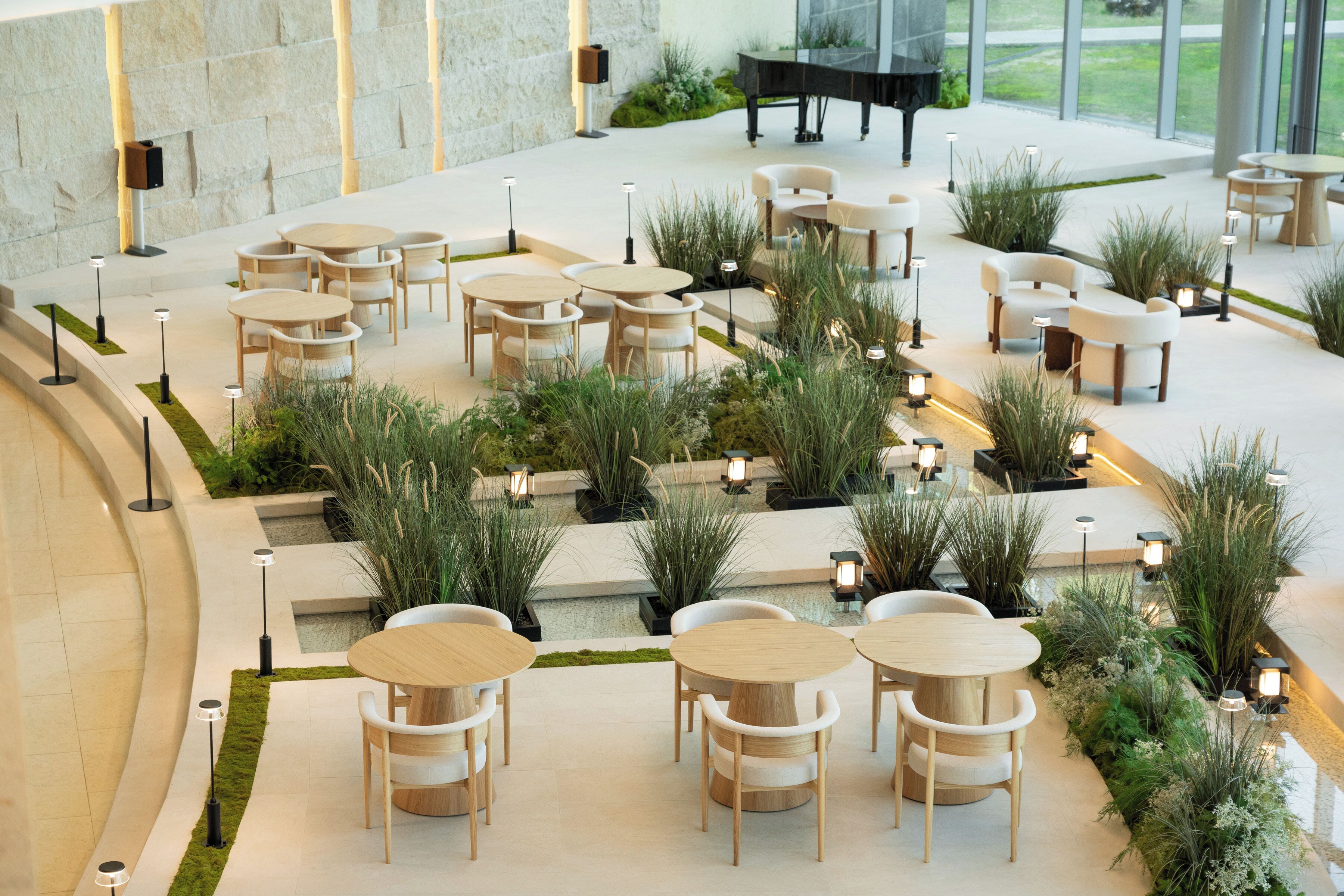 Un vaste espace extérieur aménagé avec plusieurs tables et chaises rondes, entouré d’une végétation luxuriante et éclairé par des luminaires modernes.