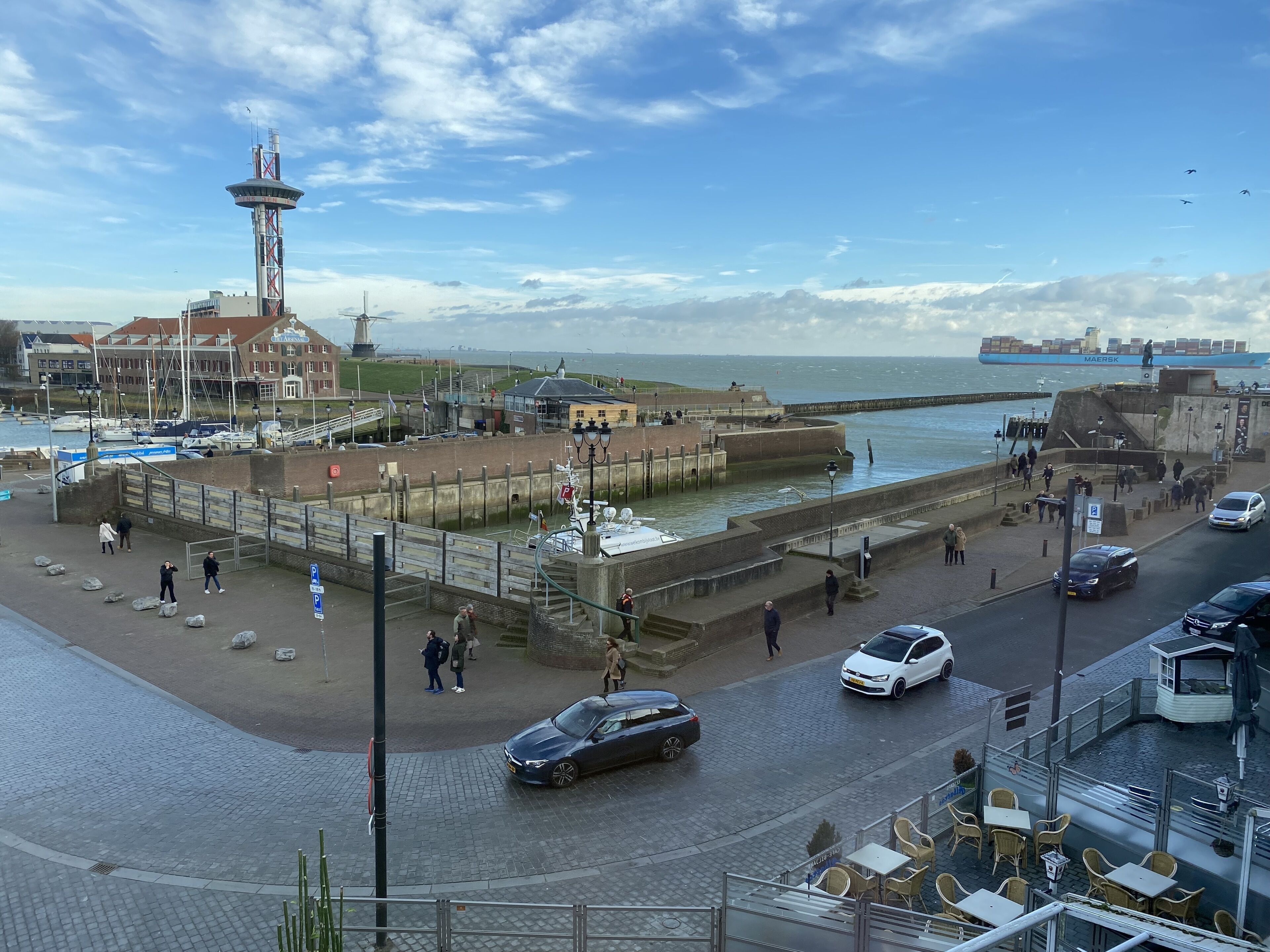 Une promenade en bord de mer avec un phare, des bateaux et un grand navire en arrière-plan.