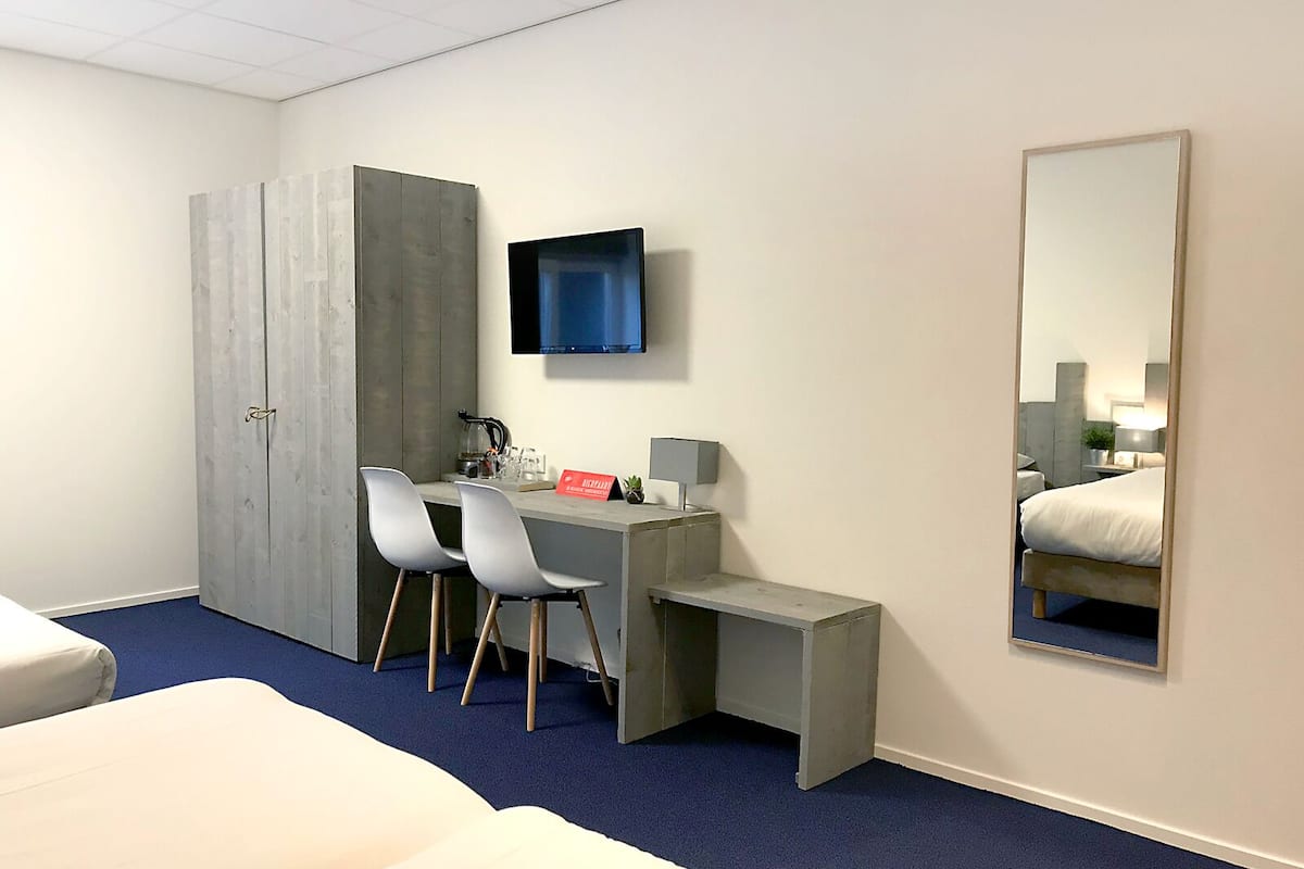 Une chambre d’hôtel comprenant un lit, un bureau avec deux chaises, une armoire, un téléviseur à écran plat et un grand miroir.