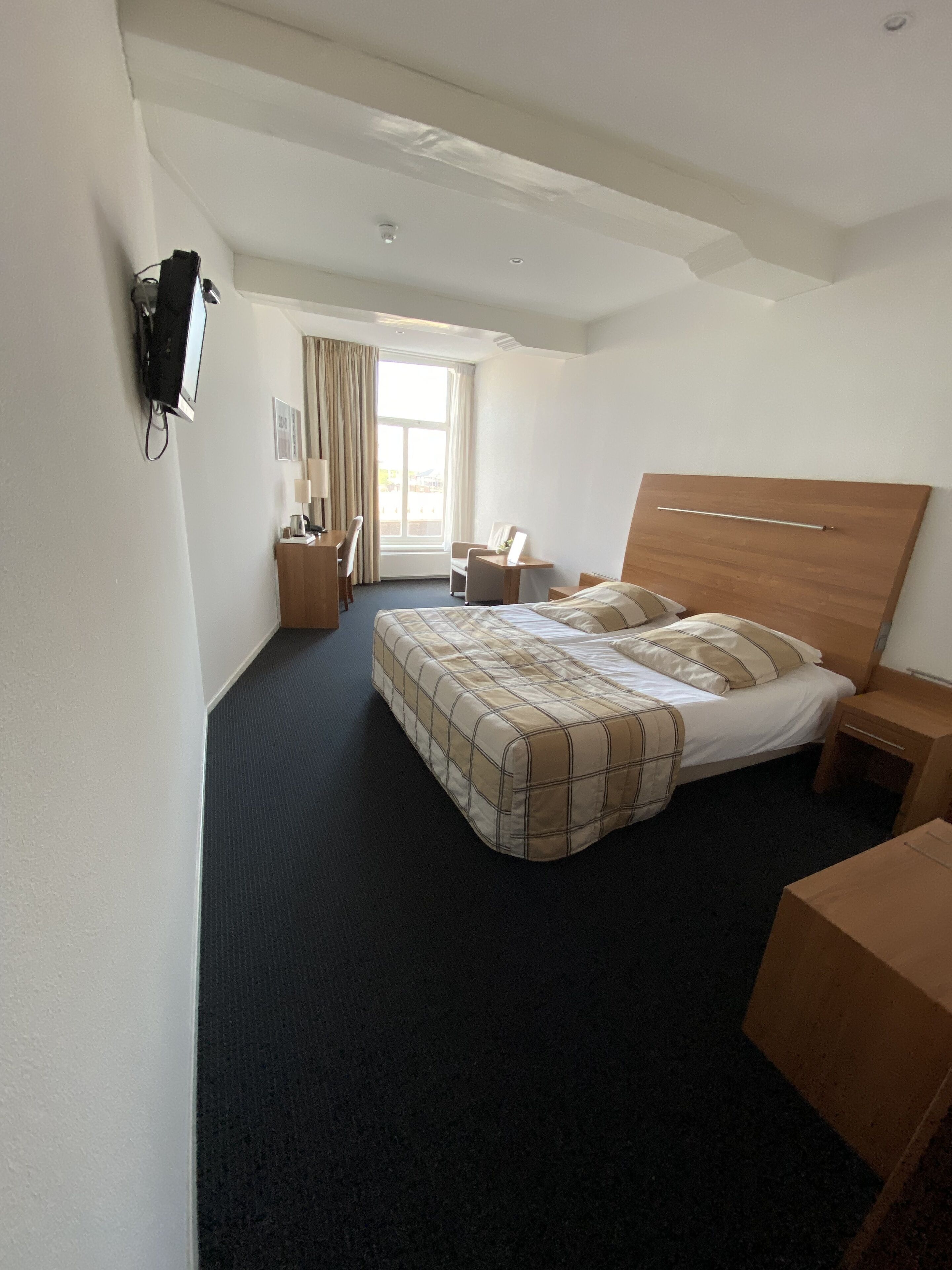 A hotel room with a bed, a desk, a chair, a TV, and a window with curtains.