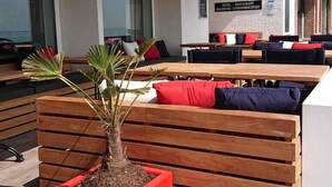 An outdoor seating area with wooden benches and a red planter with a small tree. - Hotel De Belgische Loodsensociëteit (Vlissingen)