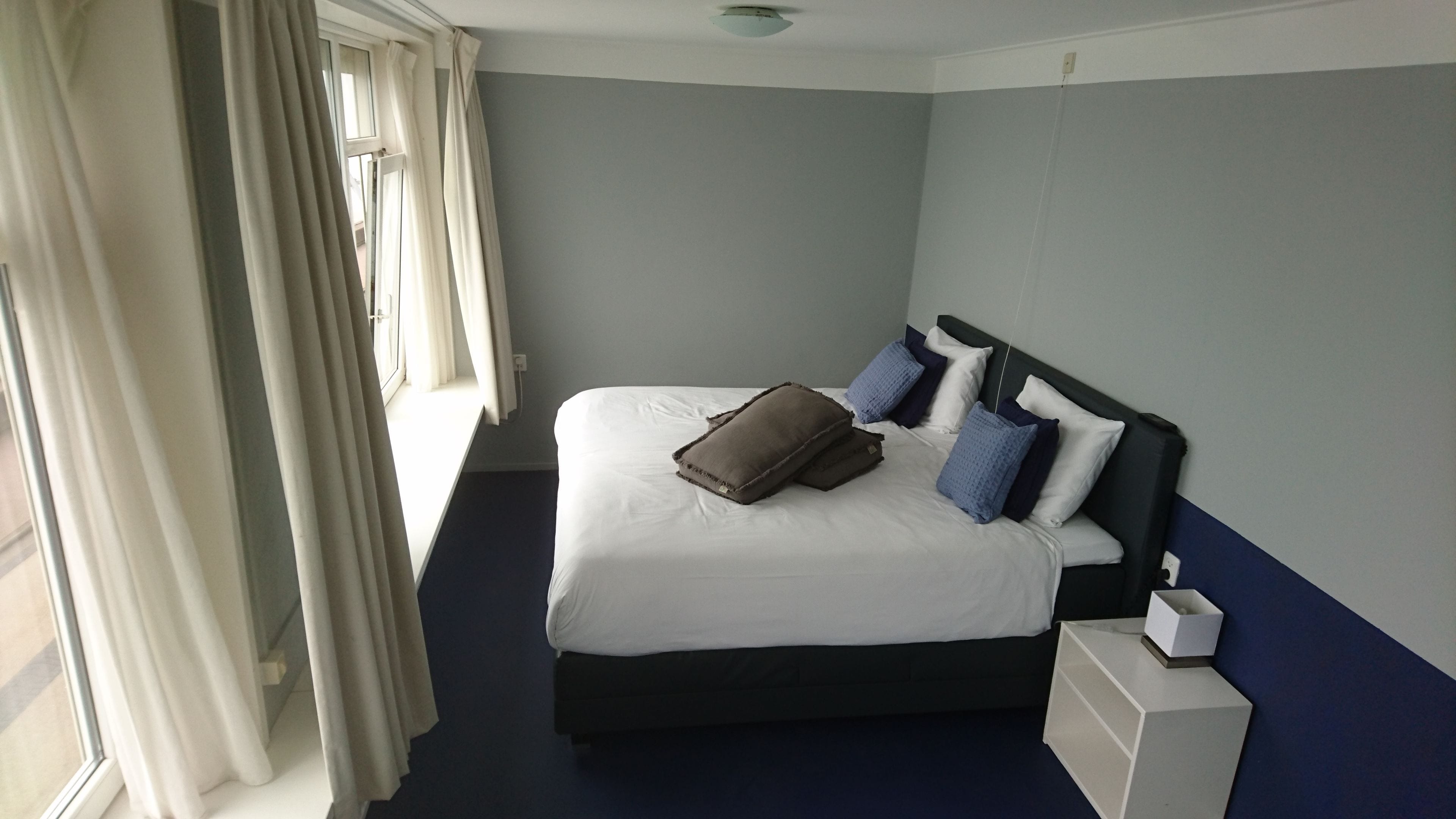 Ein Hotelzimmer mit Bett, Kissen, einem Nachttisch und einem Fenster mit Vorhängen.