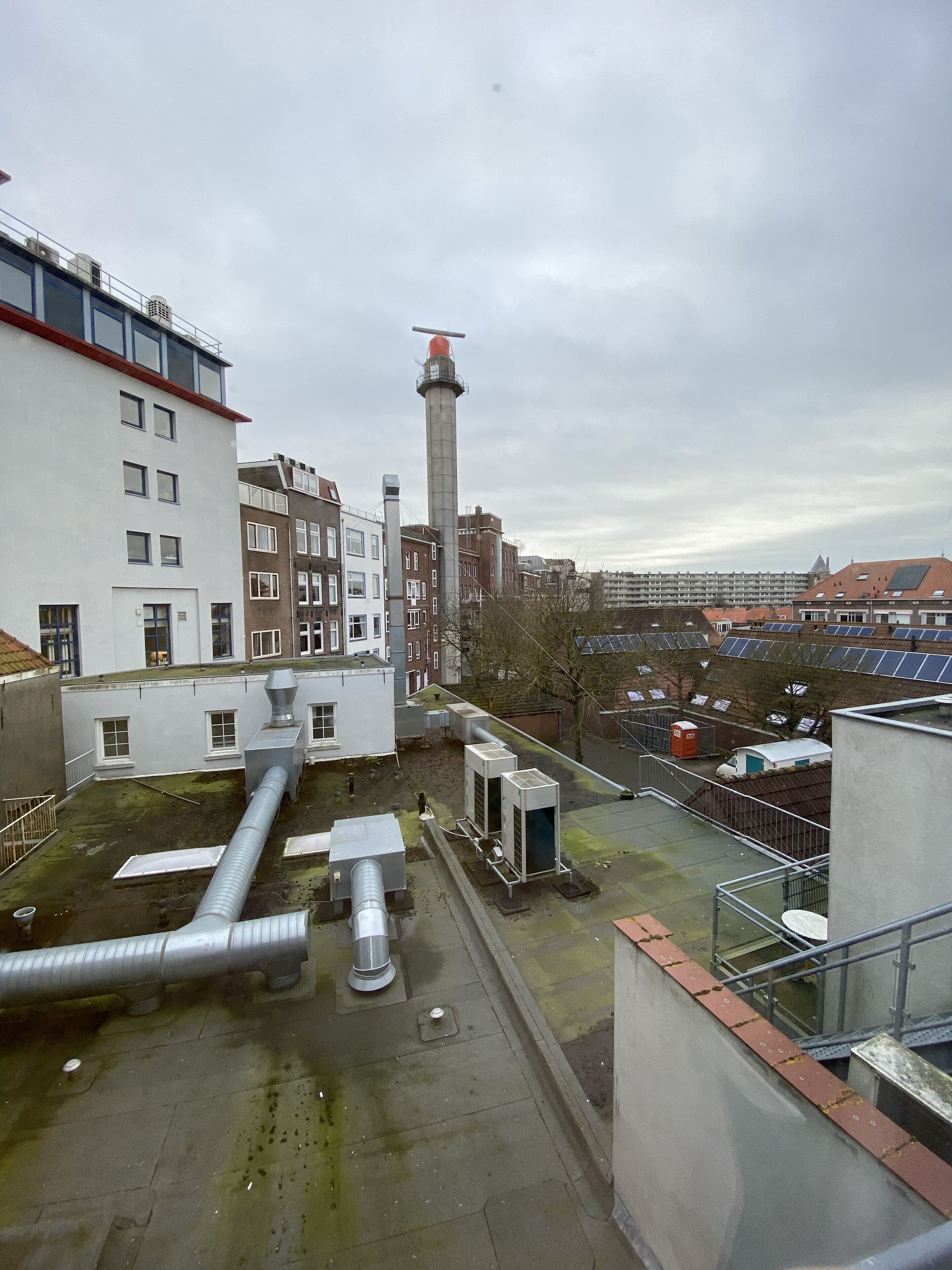 Ein Dach mit Industrieanlagen, einem hohen Schornstein und einer Reihe von Wohnhäusern im Hintergrund.