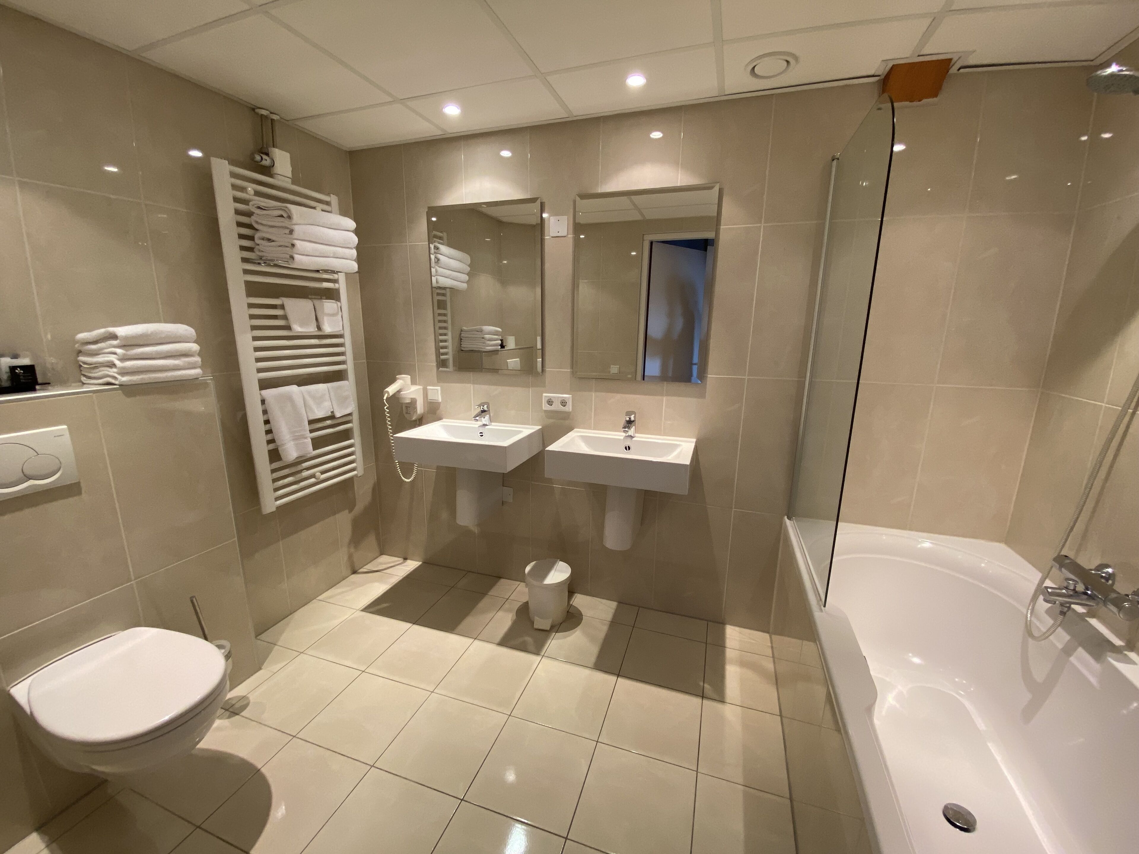 A modern bathroom with two sinks, a toilet, a bathtub, and a towel rack.