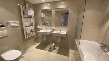 A modern bathroom with two sinks, a toilet, a bathtub, and a towel rack.