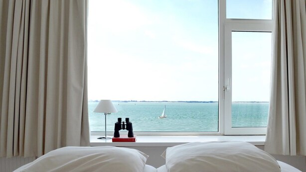 A hotel room with a bed, a window with curtains, a lamp, and binoculars on a table. - Hotel De Belgische Loodsensociëteit (Vlissingen)