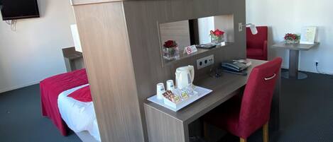 Habitación de hotel con una cama individual, un escritorio con silla, una mesita con un florero y un televisor montado en la pared.