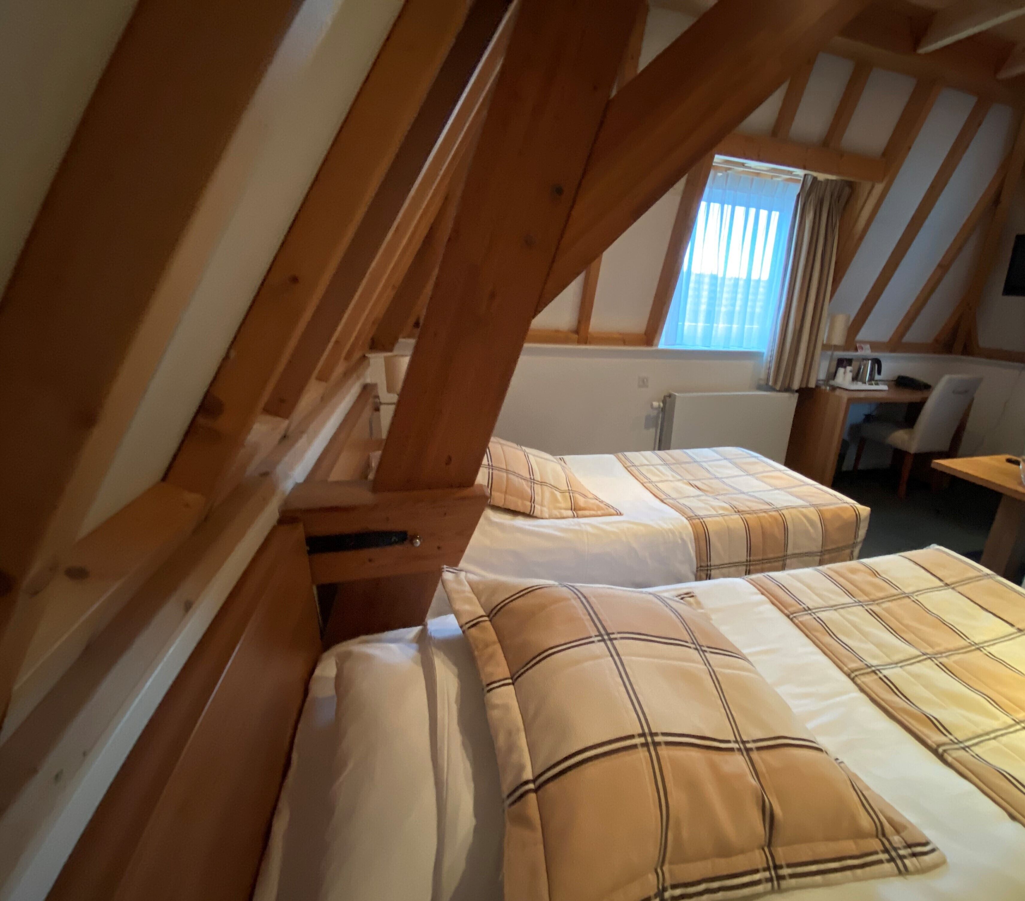 Een slaapkamer met twee bedden, houten balken, een raam met gordijnen, een bureau en een stoel.